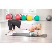 Blondes weibliches Model in Sportkleidung führt eine Übung mit der Faszienrolle duch. 
